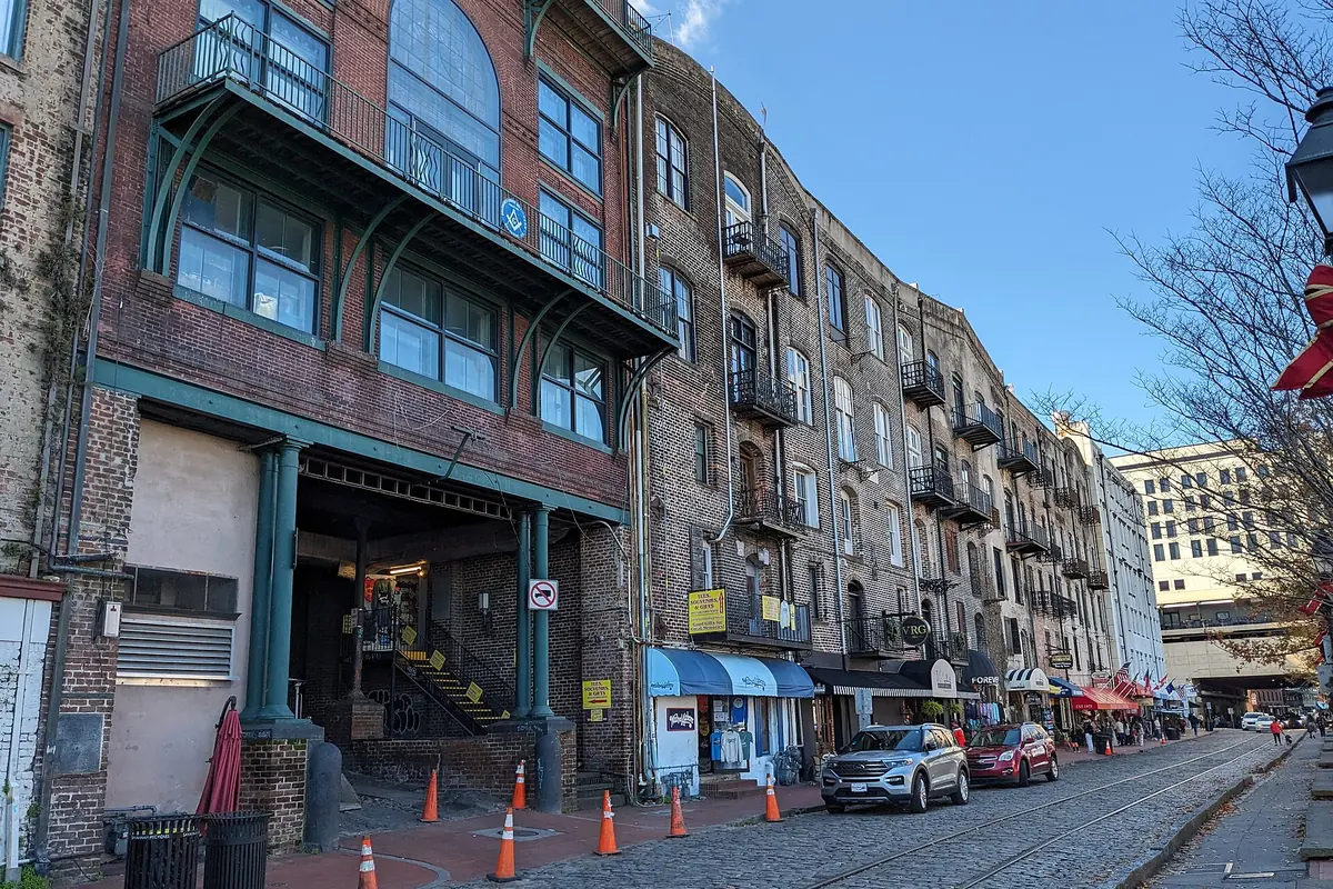 A row of brick former cotton warehouses along River Street, with iron balconies, shopfronts and cobbles with old tramlines.