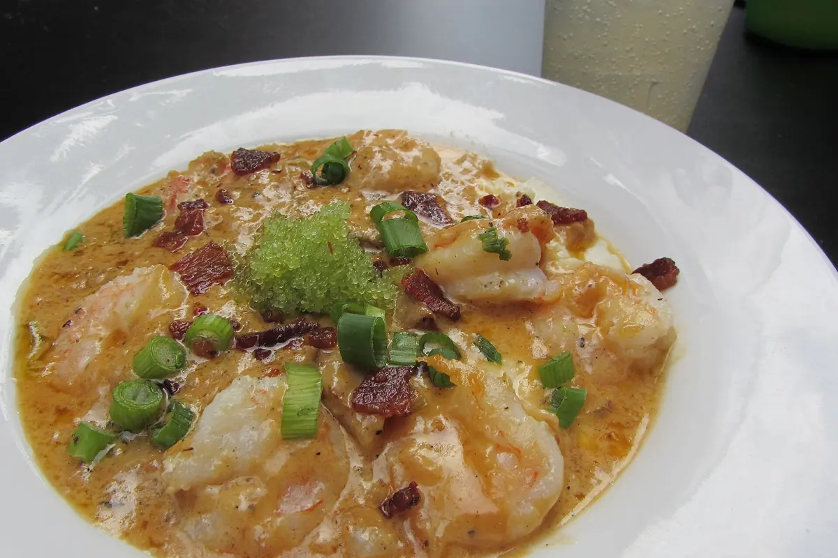 A white bowl of shrimp and grits topped with bacon and scallions, photographed at a restaurant in New Orleans.
